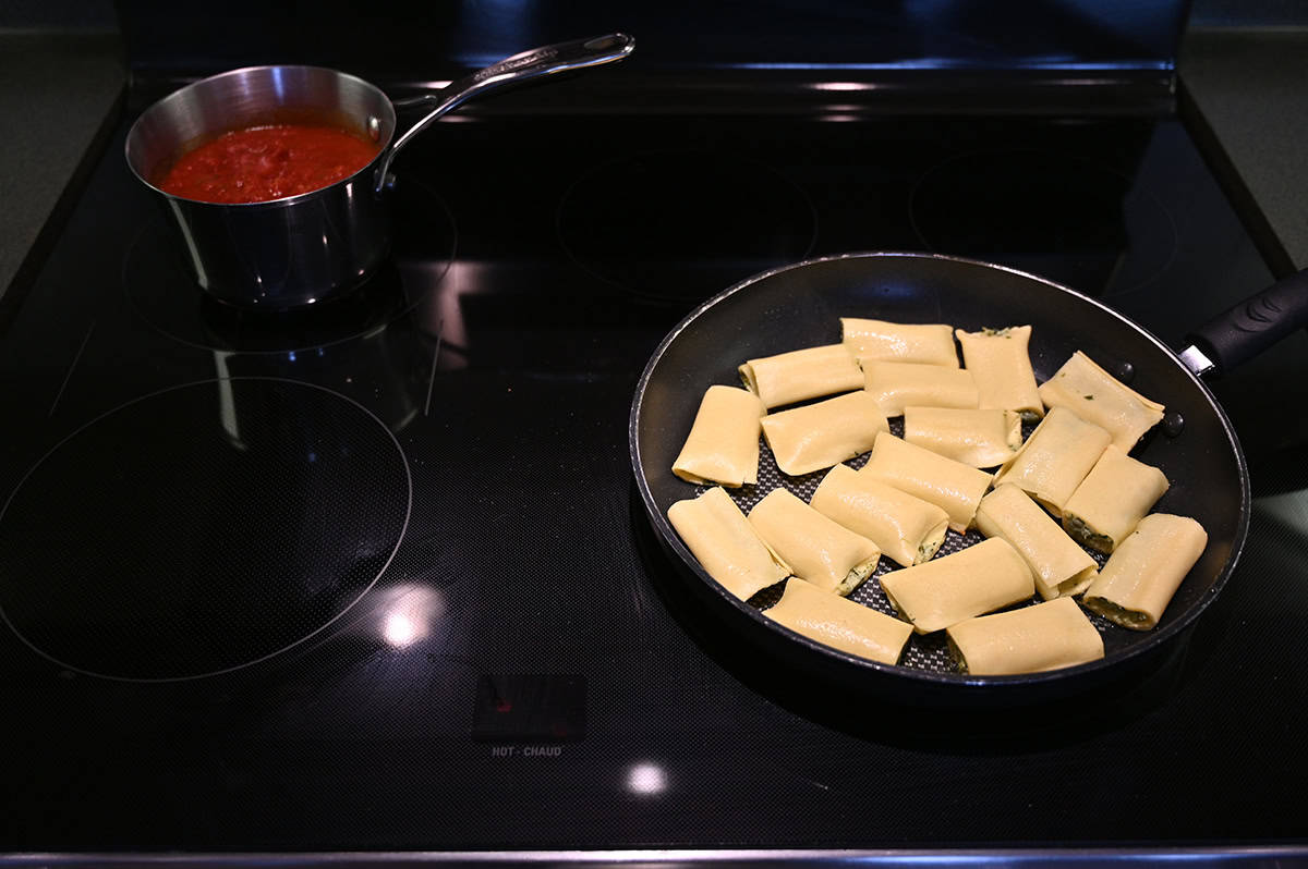 Image of the cannelloni cooking in a frying pan on top of the stove beside a pot of red sauce.