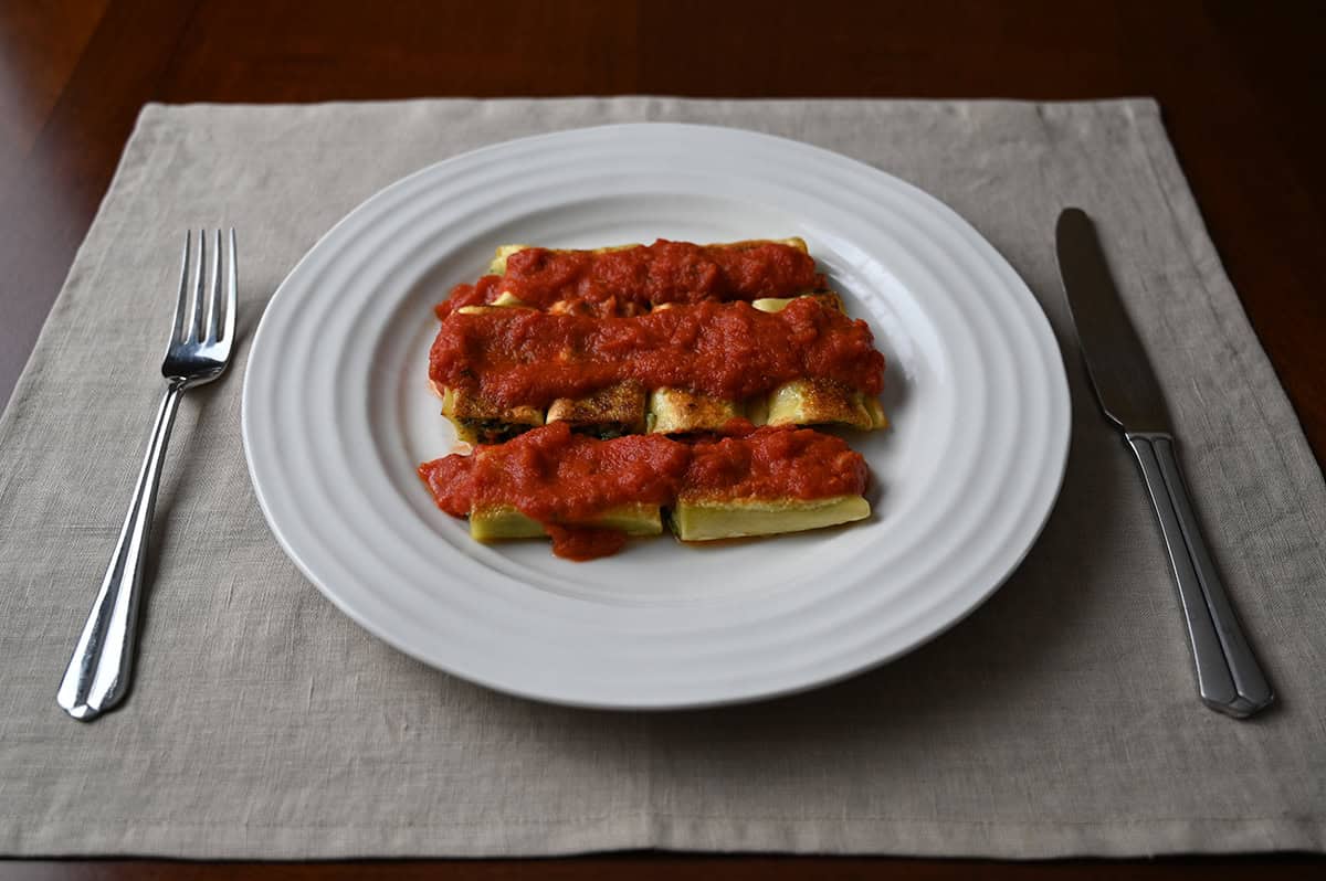 Top down side view image of a plate with cannelloni served on it with red sauce on top of the cannelloni.