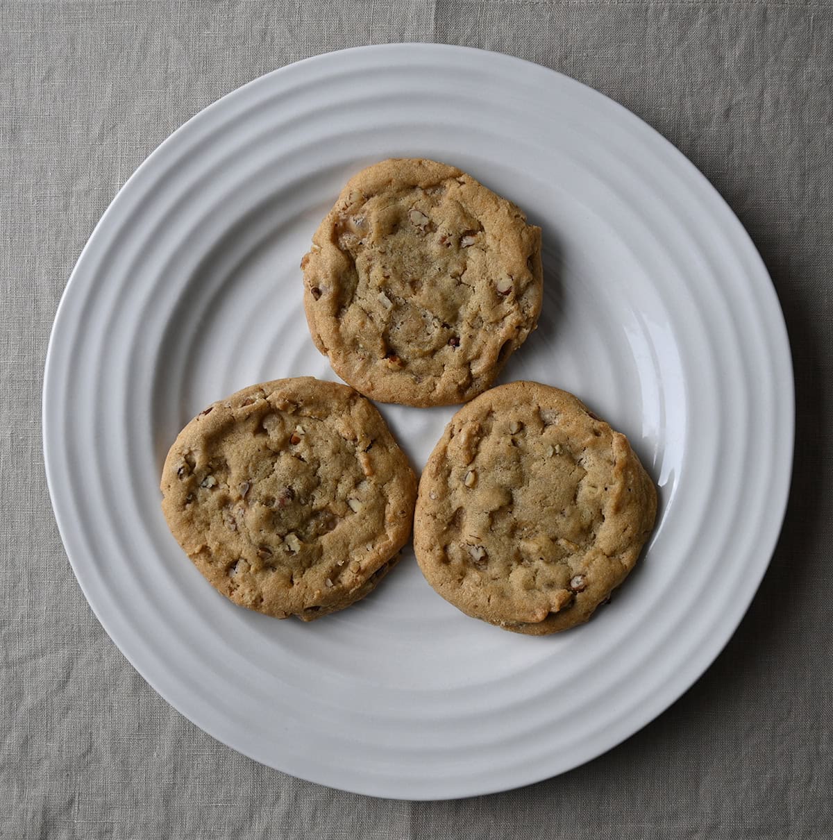 Top down image of a white plate with three maple pecan cookies served on it.