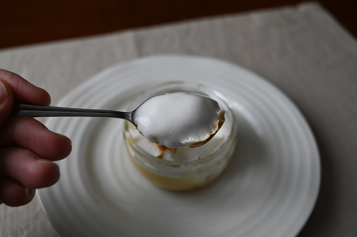Image of a spoon with meringue topping on it hovering over a lemon meringue pie ramekin.