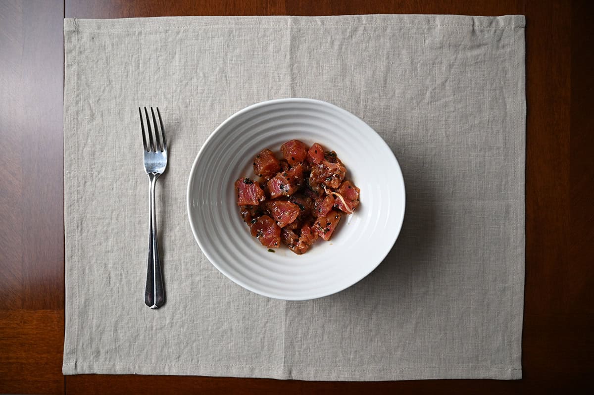 Top down image of a bowl of tuna poke sitting on a table beside a fork.