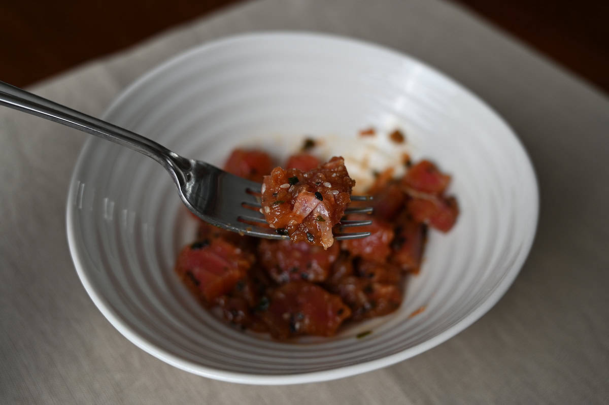 Closeup image of a fork with some tuna gristly poke on it hovering over a bowl of poke.