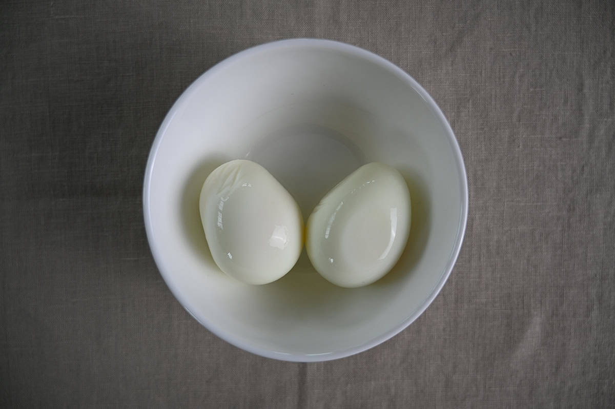 Top down image of two hard boiled eggs served in a white bowl.