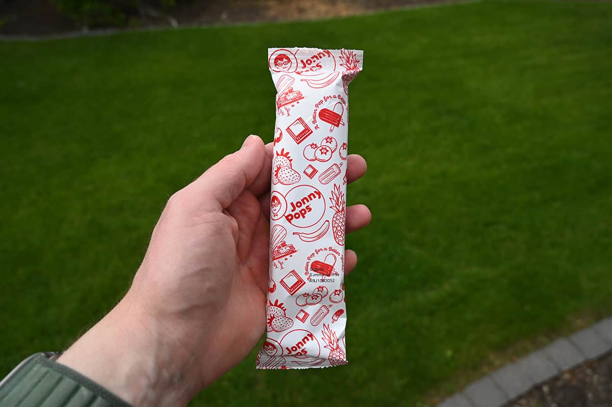 Image of a hand holding one Jonny pop in its wrapper close to the camera. 
