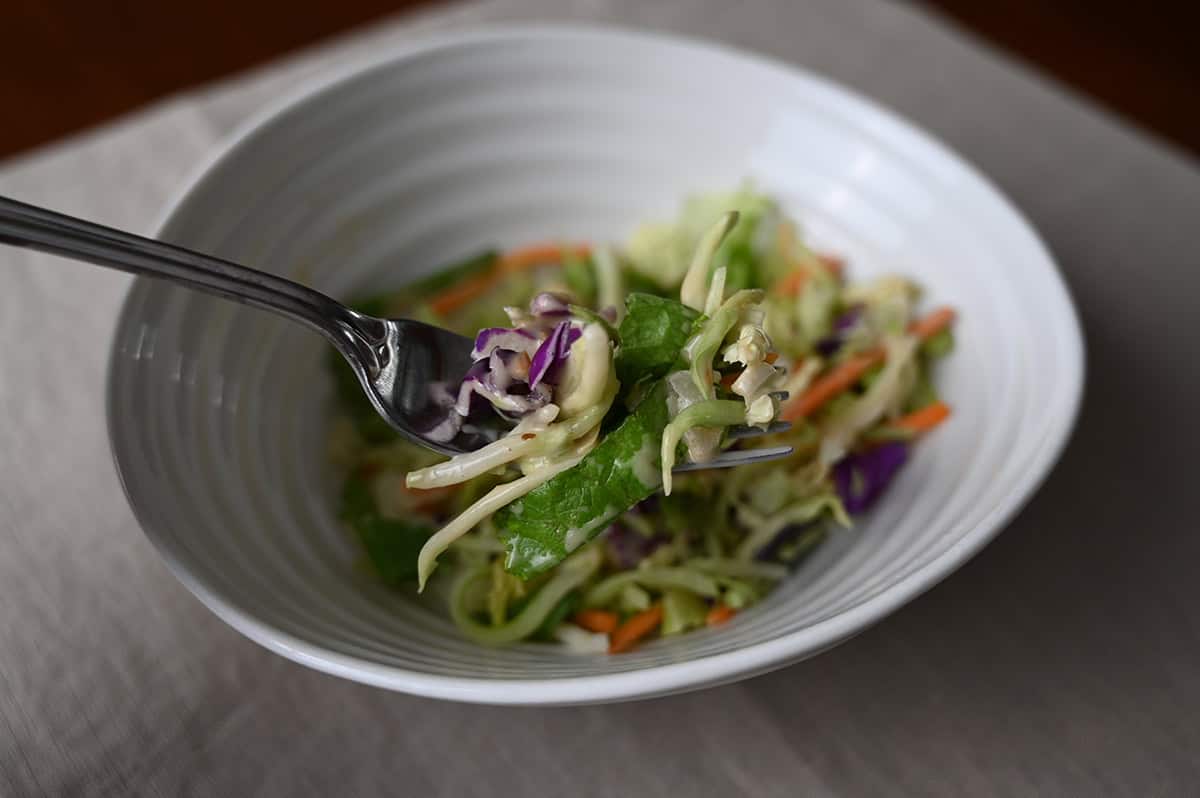 Closeup image of a fork with salad on it hovering over a white bowl filled with salad.
