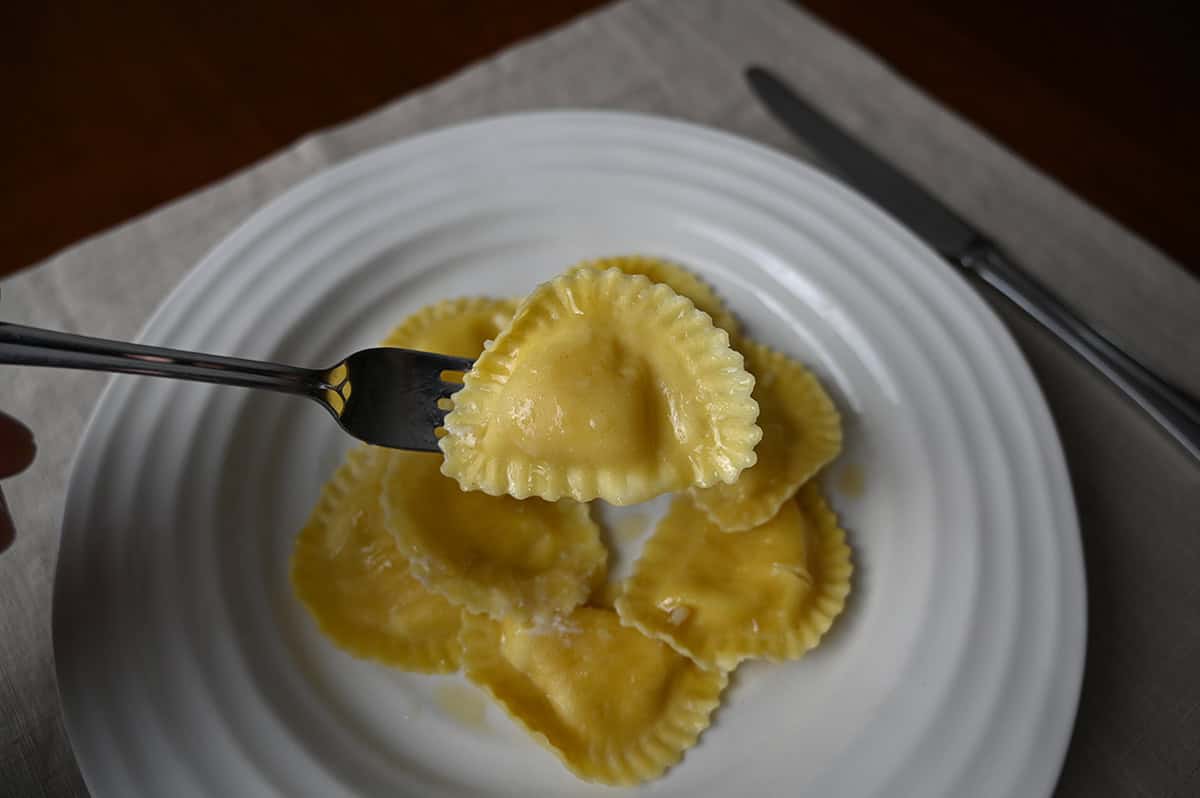 Image of a fork with one whole piece of ravioli resting it above a plate of ravioli.