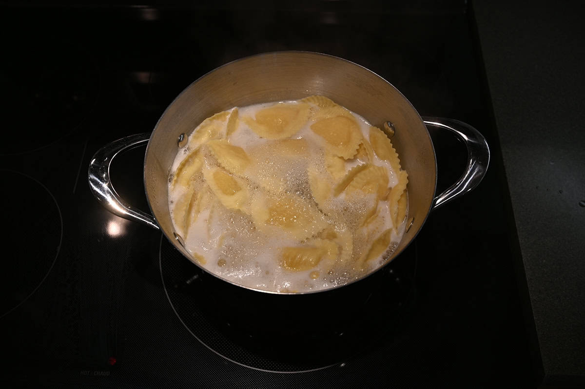 Top down image of a pot of boiling water with ravioli being cooked in the boiling water.