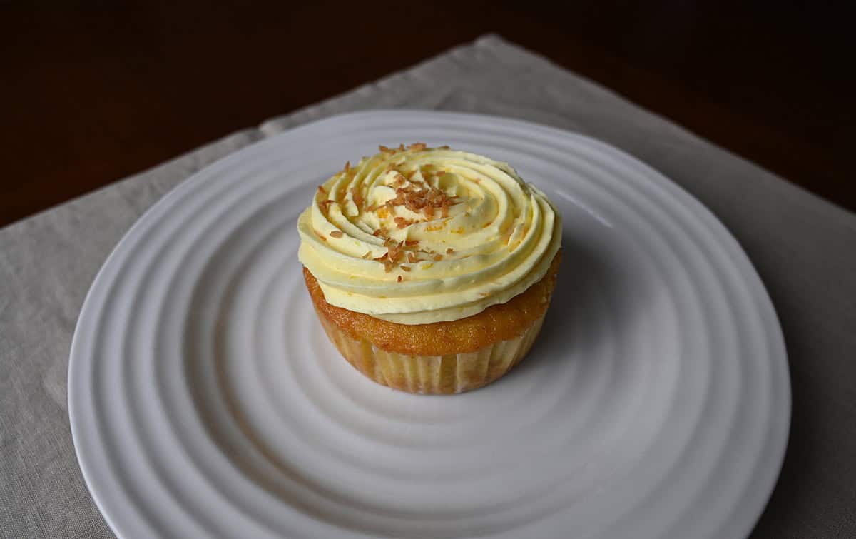 Side view closeup image of one mini pineapple coconut mini cake still in the wrapper and served on a white plate. 