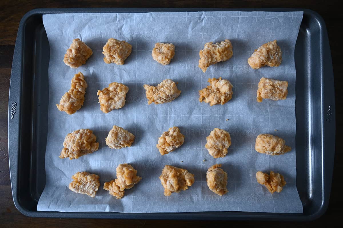 Top down image of frozen chicken chunks spread out on a cookie sheet before baking in the oven.