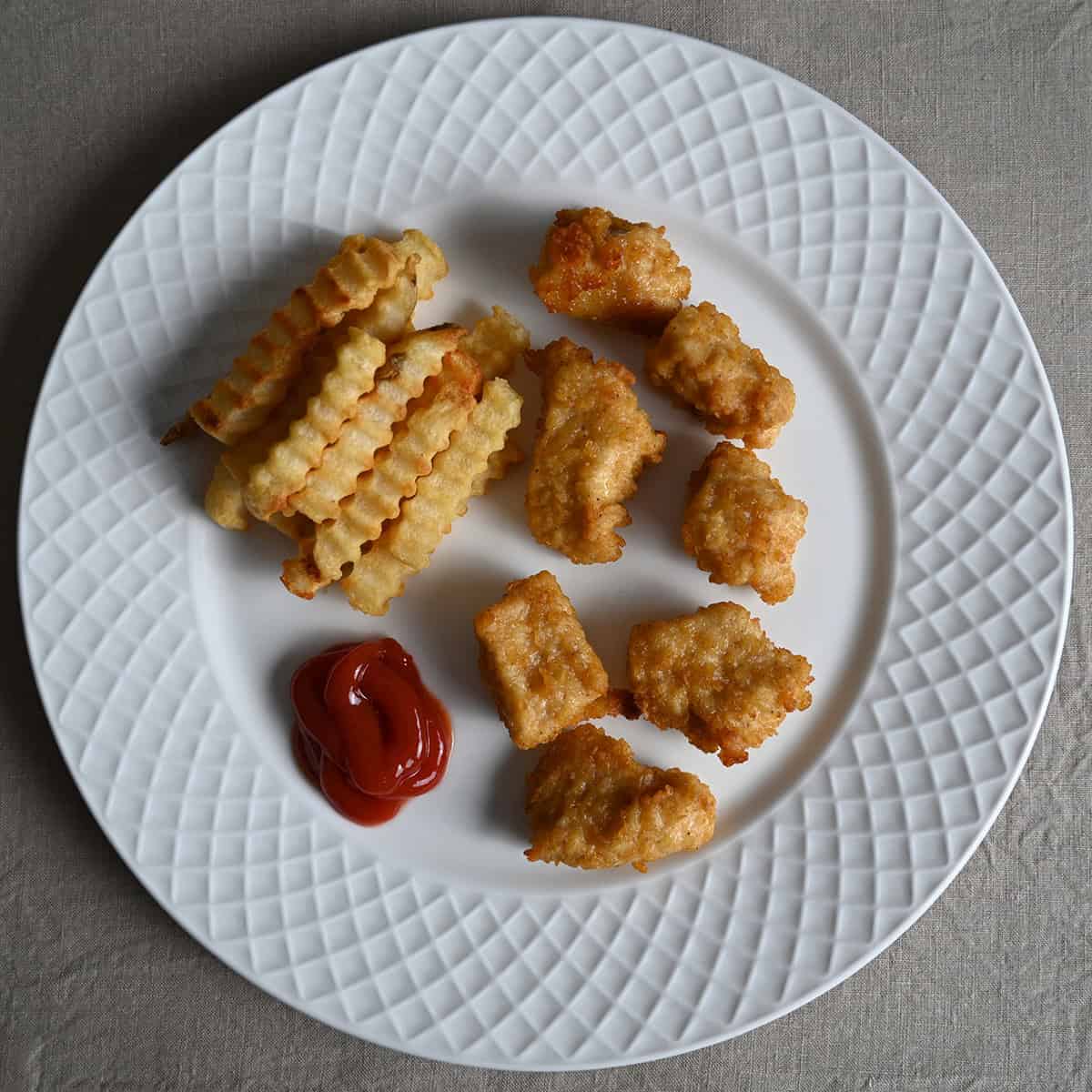 Top down image of a white plate with fries, ketchup and chicken breast chunks on the plate.