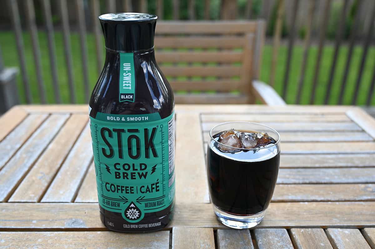 Image of the bottle of Stok cold brew sitting on a table beside a full glass of cold brew with ice in it,