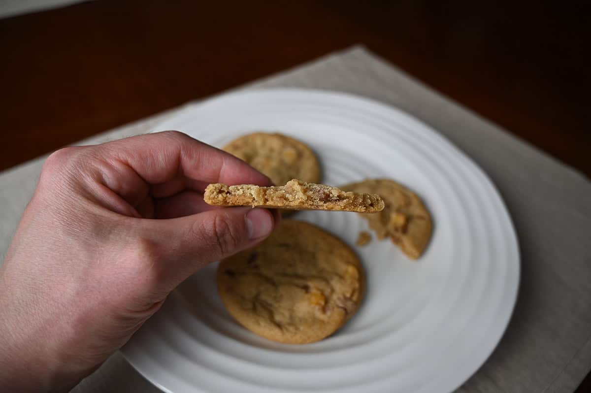 Closeup image of a hand holding on cookie with a few bites taken out of it so you can see the center.