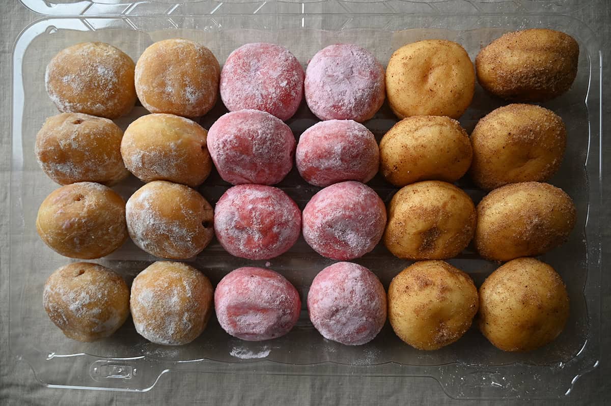 Top down image of a plastic container of donuts opened showing 24 mini donuts in three different flavors.