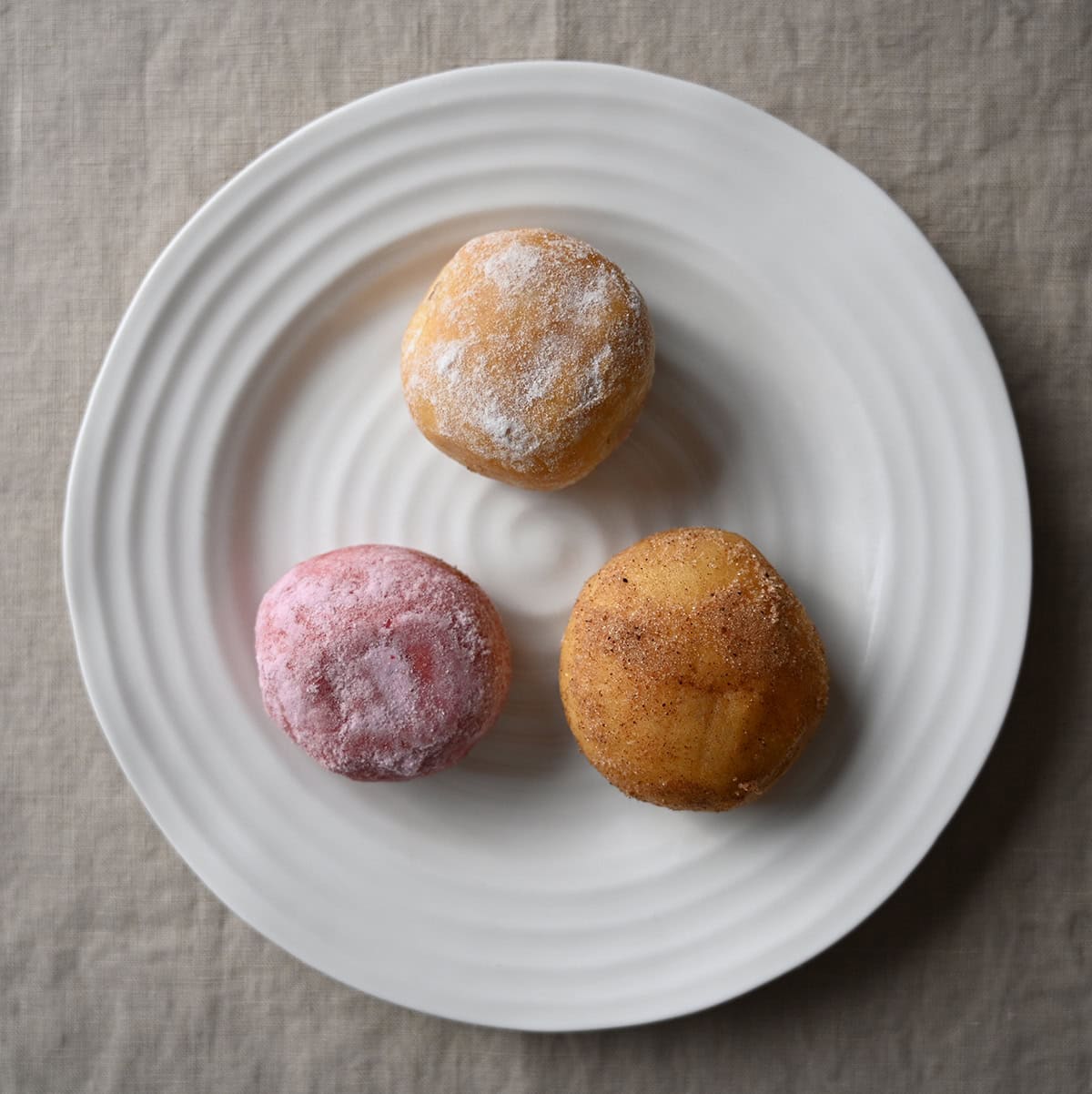 Image of a plate with three different kinds of mini donuts served on it.