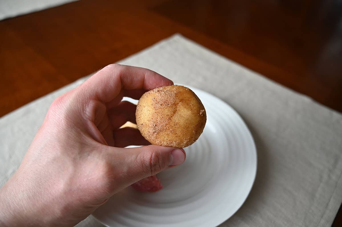 Image of a hand holding one apple cinnamon donut close to the camera.