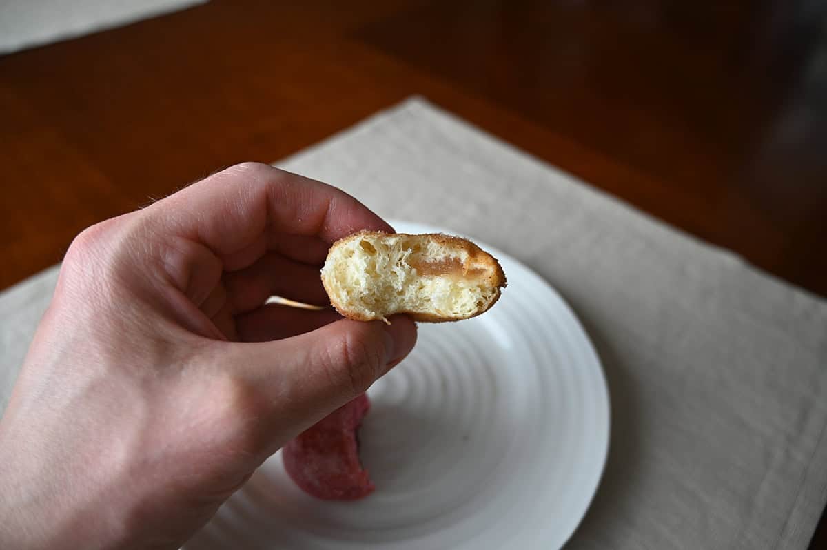 Image of a hand holding one apple cinnamon mini donut with a bite taken  out of it so you can see the middle. 