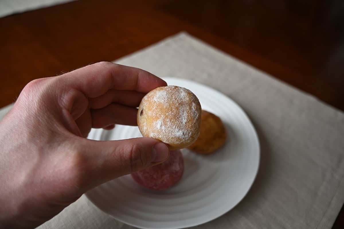 Image of a hand holding one chocolate hazelnut mini donut close to the camera.