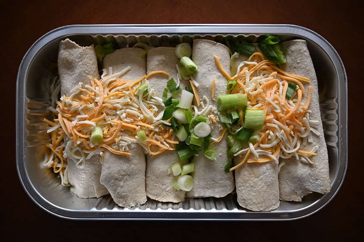 Image of the enchiladas tray opened, uncooked and sitting on a table. You can see six enchiladas in the tray.