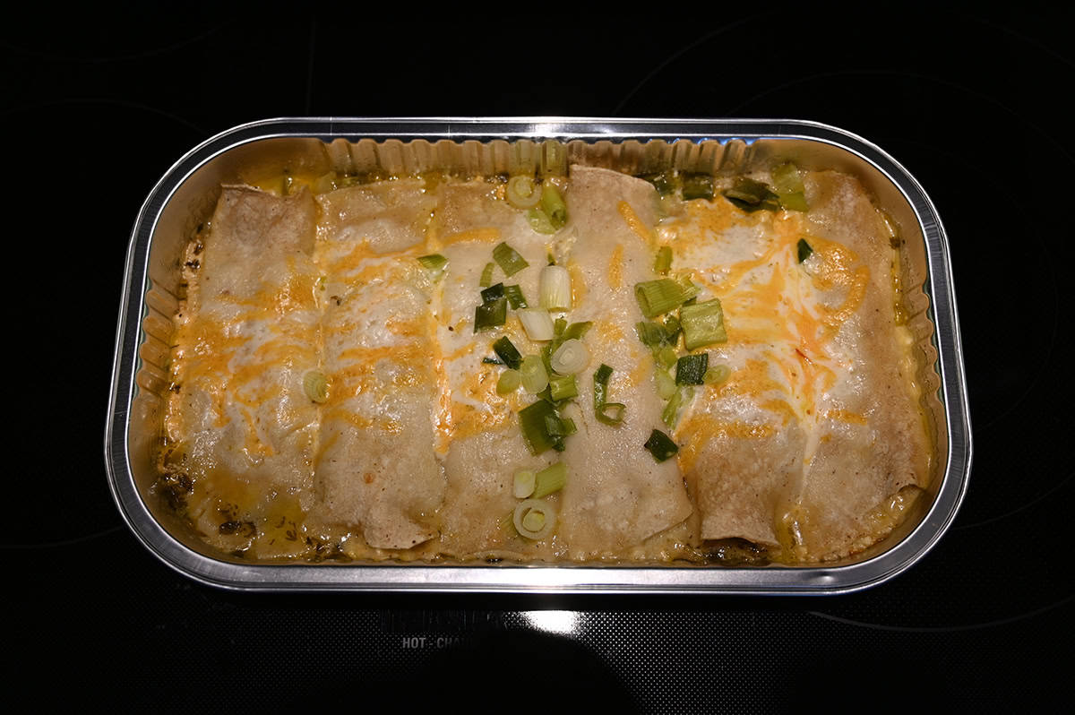 Image of a tray of cooked enchiladas with cheese on top sitting on an oven.