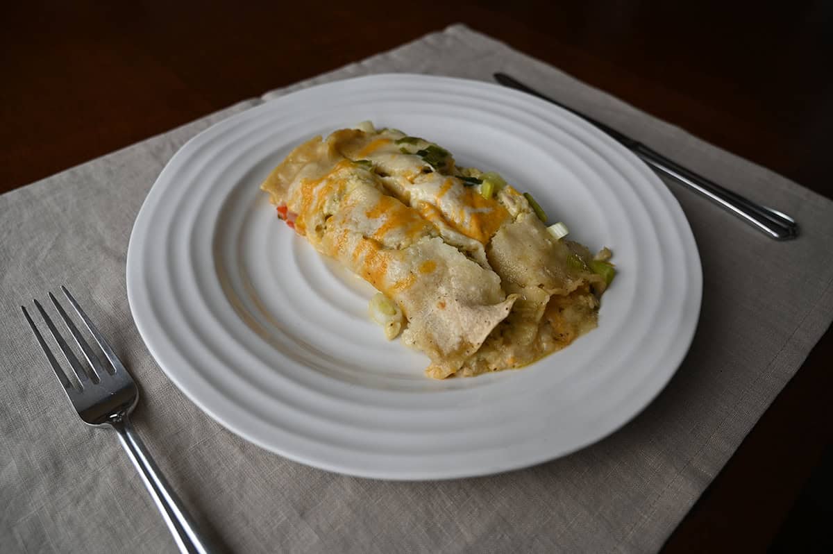 Image of two cooked enchiladas served on a white plate, there is a fork and knife beside the plate.