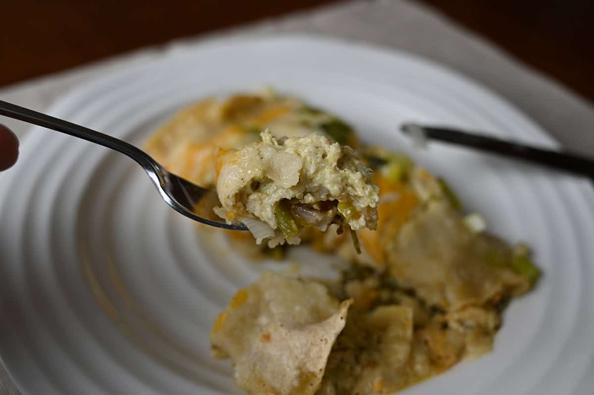 Closeup image of a fork with a bite of enchilada on it. In the background of the image is a plate with an enchilada on it.