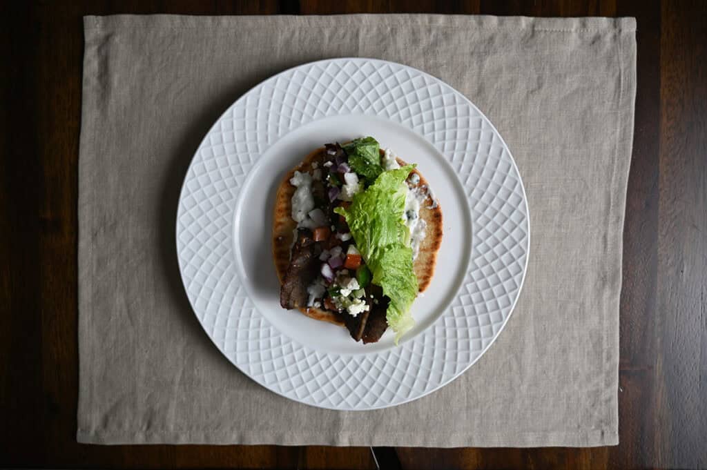 Top down image of one gyro open faced with all the ingredients on it served on a white plate. 