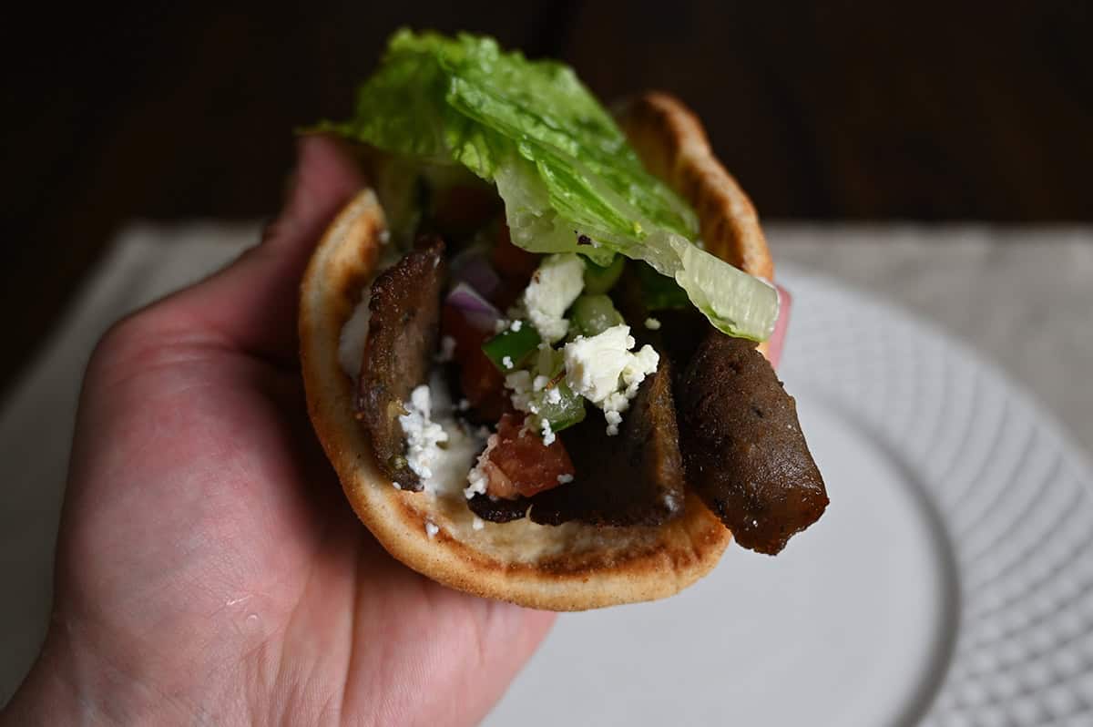 Closeup image of a hand holding one gyro on it's side close to the camera so you can see the ingredients inside. 