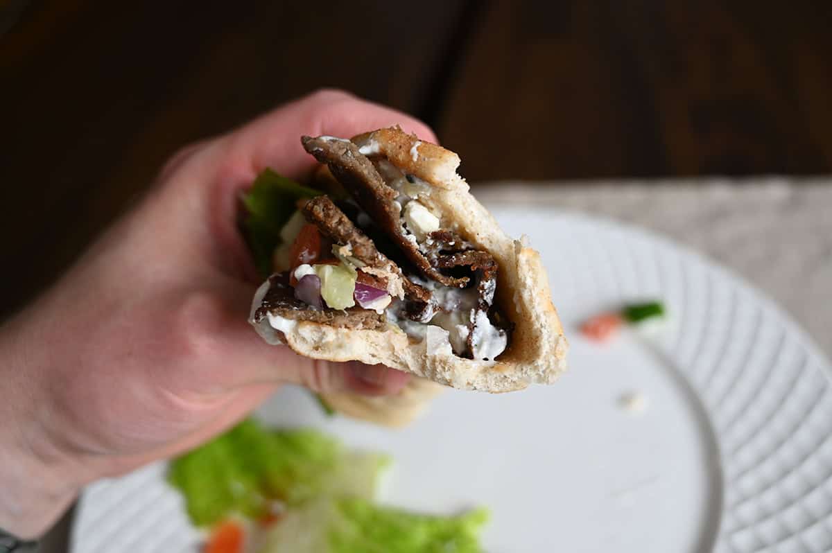 Sideview closeup image of a hand holding one gyro with a few bites taken out of it. 