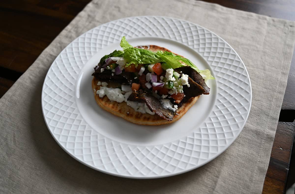 Sideview top down image of one gyro open faced with all the ingredients on it served on a white plate. 