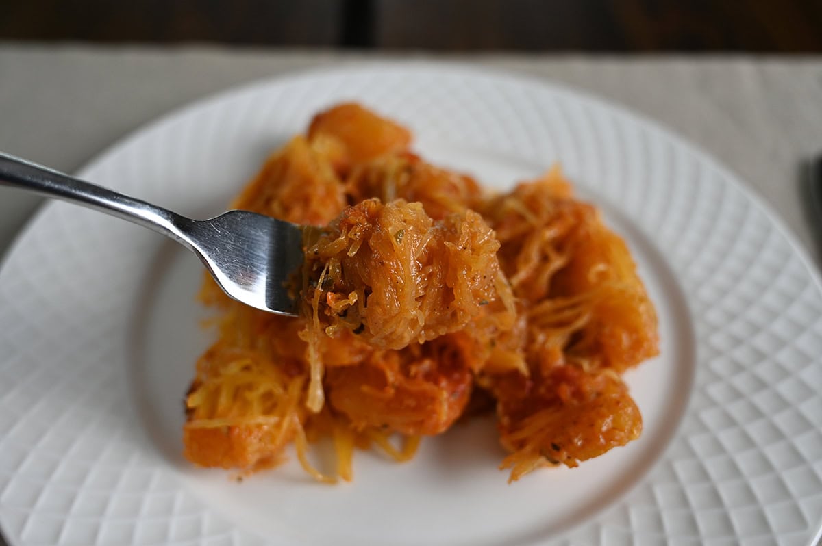 Closeup side view image of a fork with spaghetti squash on it, in the background is a plate of spaghetti squash.