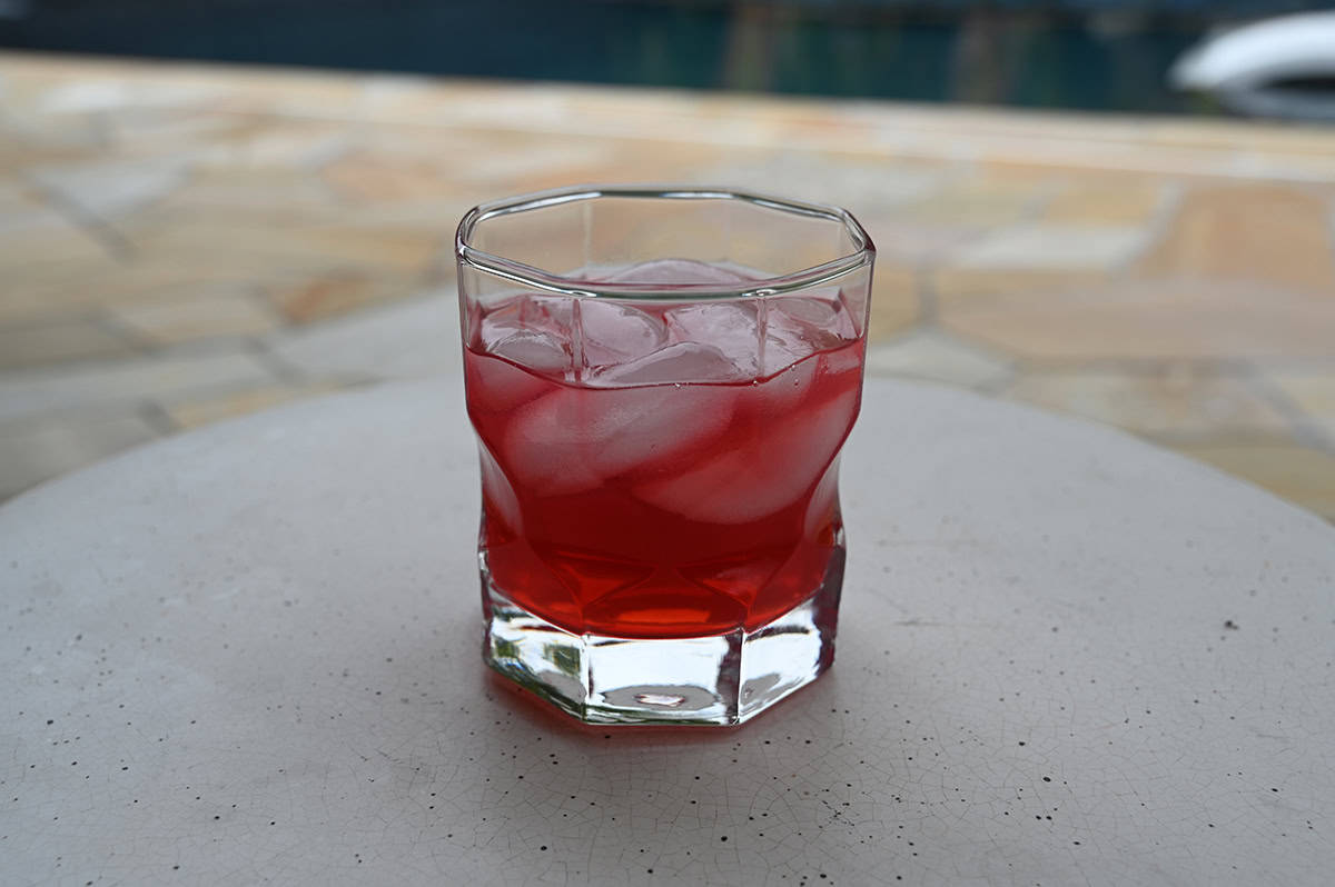 Image of one poured glass of spiced cranberry margarita wine cocktail sitting on a table outside.