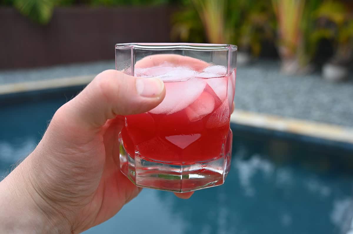 Image of a hand holding one glass of spiced cranberry margarita up close to the camera with a pool in the background.