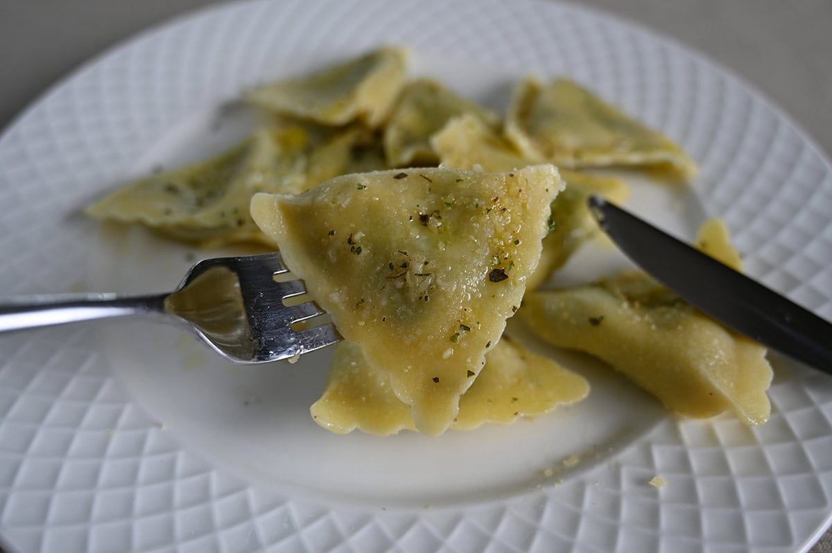 Closeup image of one triangle shaped ravioli on a fork with a plate of ravioli in the background.