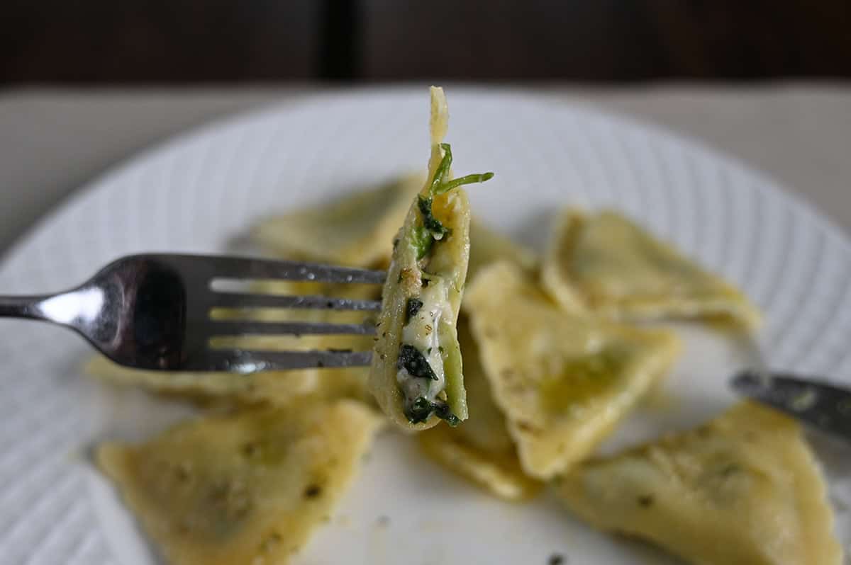 Closeup image of one ravioli on a fork with a bite taken out of it so you can see the filling. 