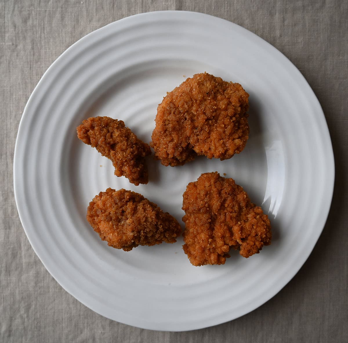 Top down image of four chicken tenders served on a white plate.