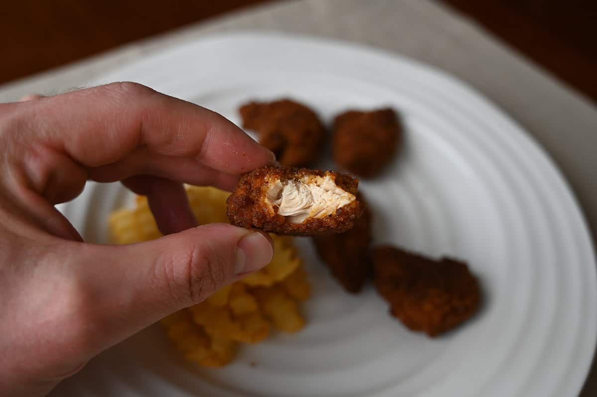 Closeup image of a hand holding one cooked tender with a bite taken out of it so you can see the inside.