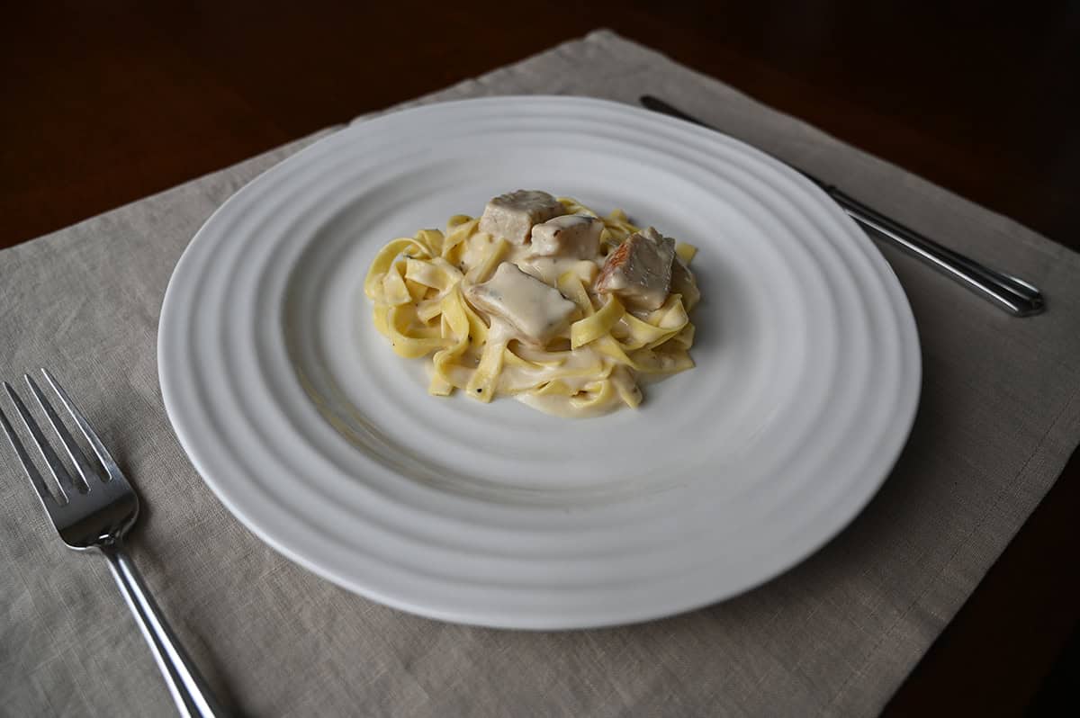 Side view image of the fettuccine alfredo served on a white plate with chicken on top of it. 