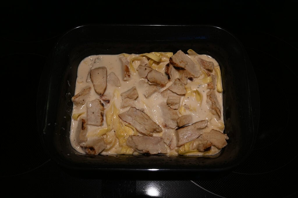 Image of a tray of fettuccine with chicken and alfredo sauce sitting on a stovetop.
