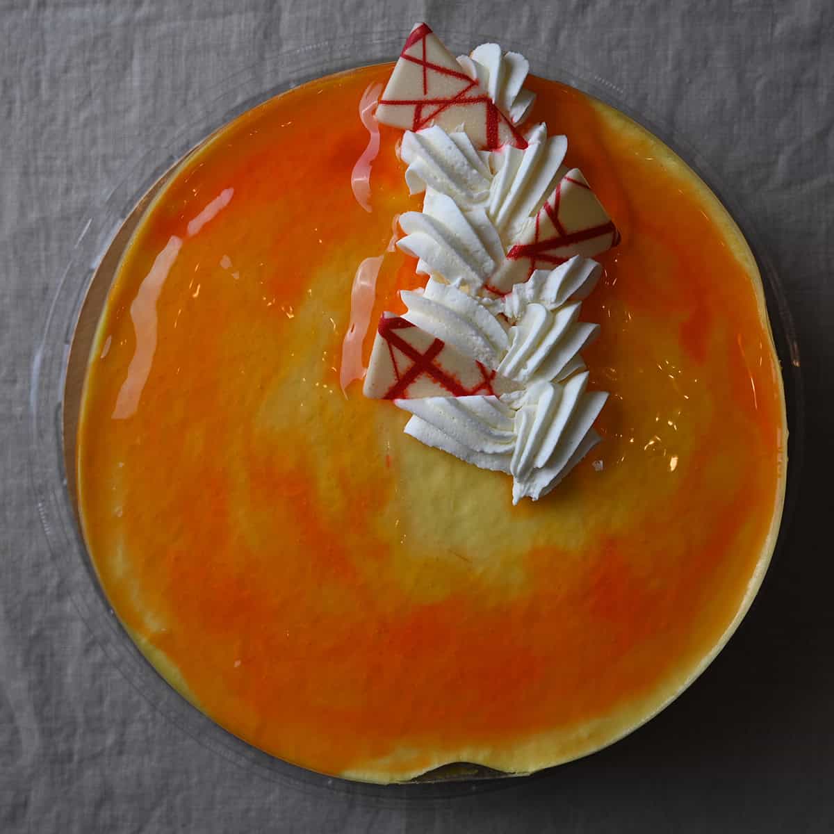 Top down image of the mango passionfruit mousse cake showing the glaze on top, some vanilla icing and a few decorative white chocolate pieces.