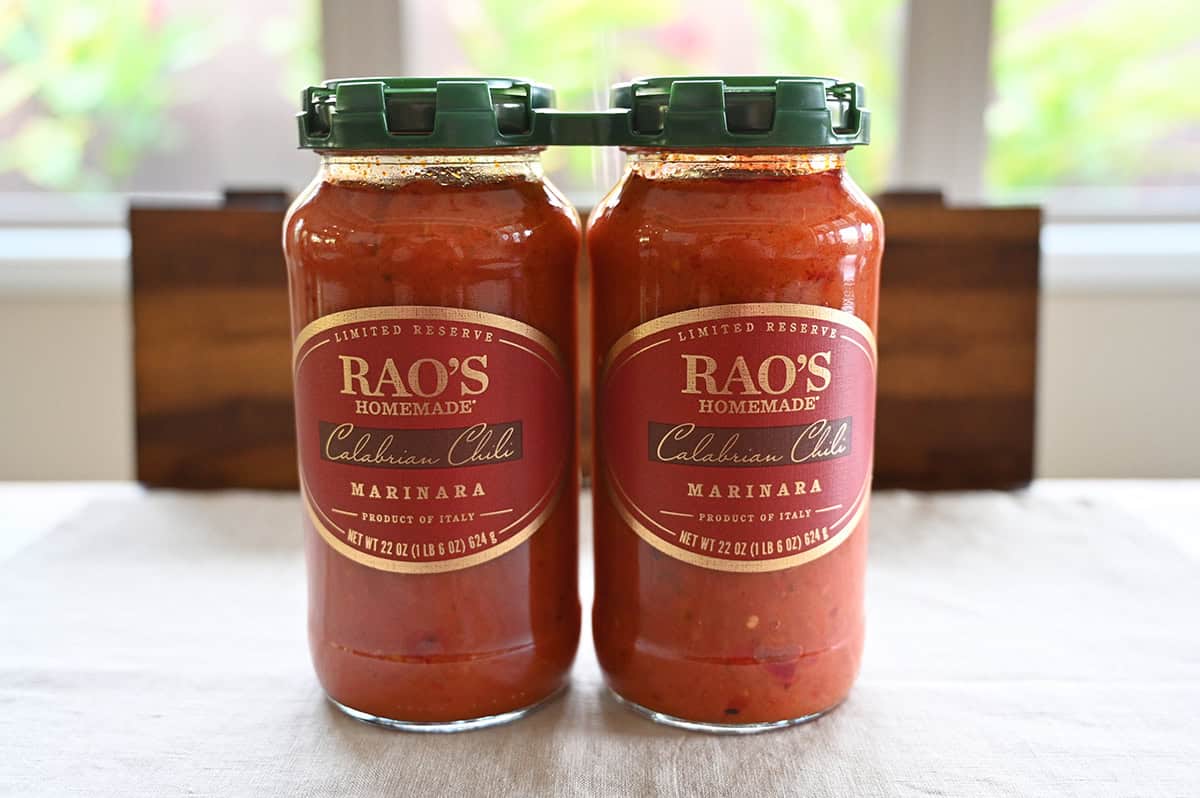 Image of two jars of sauce beside standing beside one another on a table unopened.