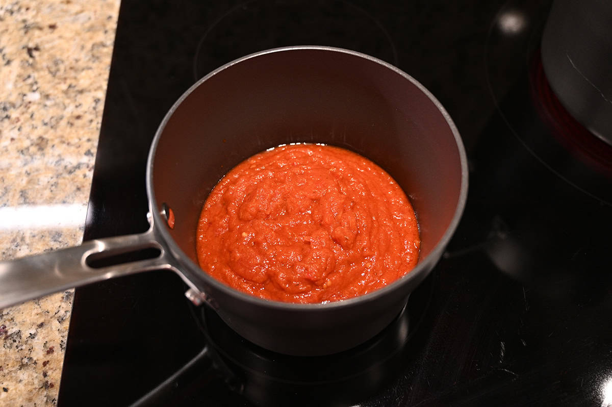 Image of a pot with marinara sauce on it being heated on a stovetop. 