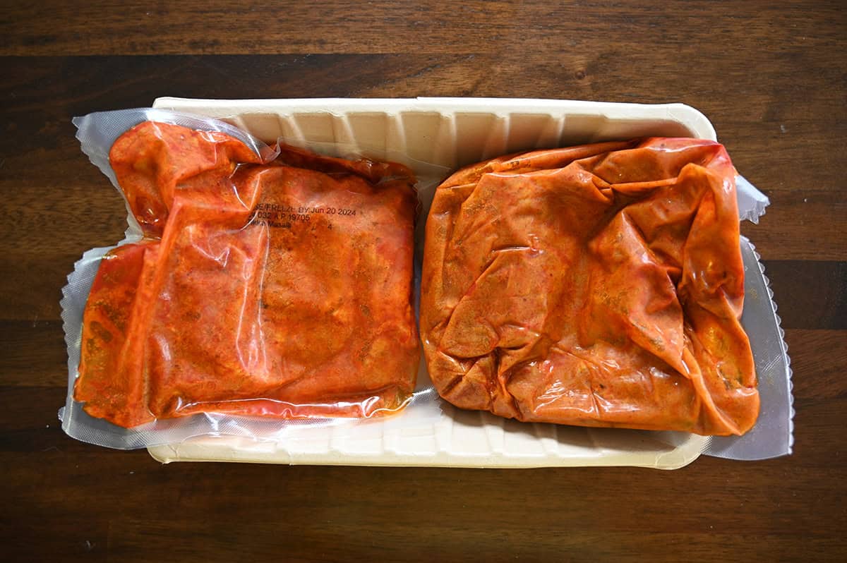 Top down image of two sealed pouches of tikka masala sitting in a plastic rectangular container.