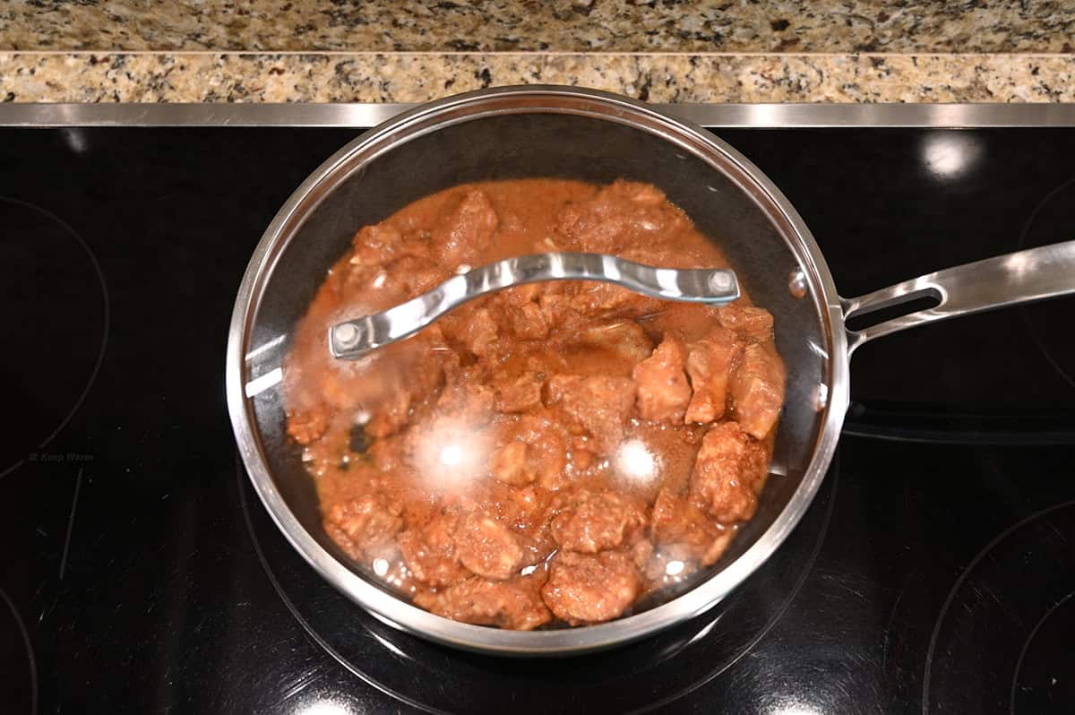 Top down image of a pot with a clear lid on sitting on a stovetop, inside the pot is tikka masala being heated. 