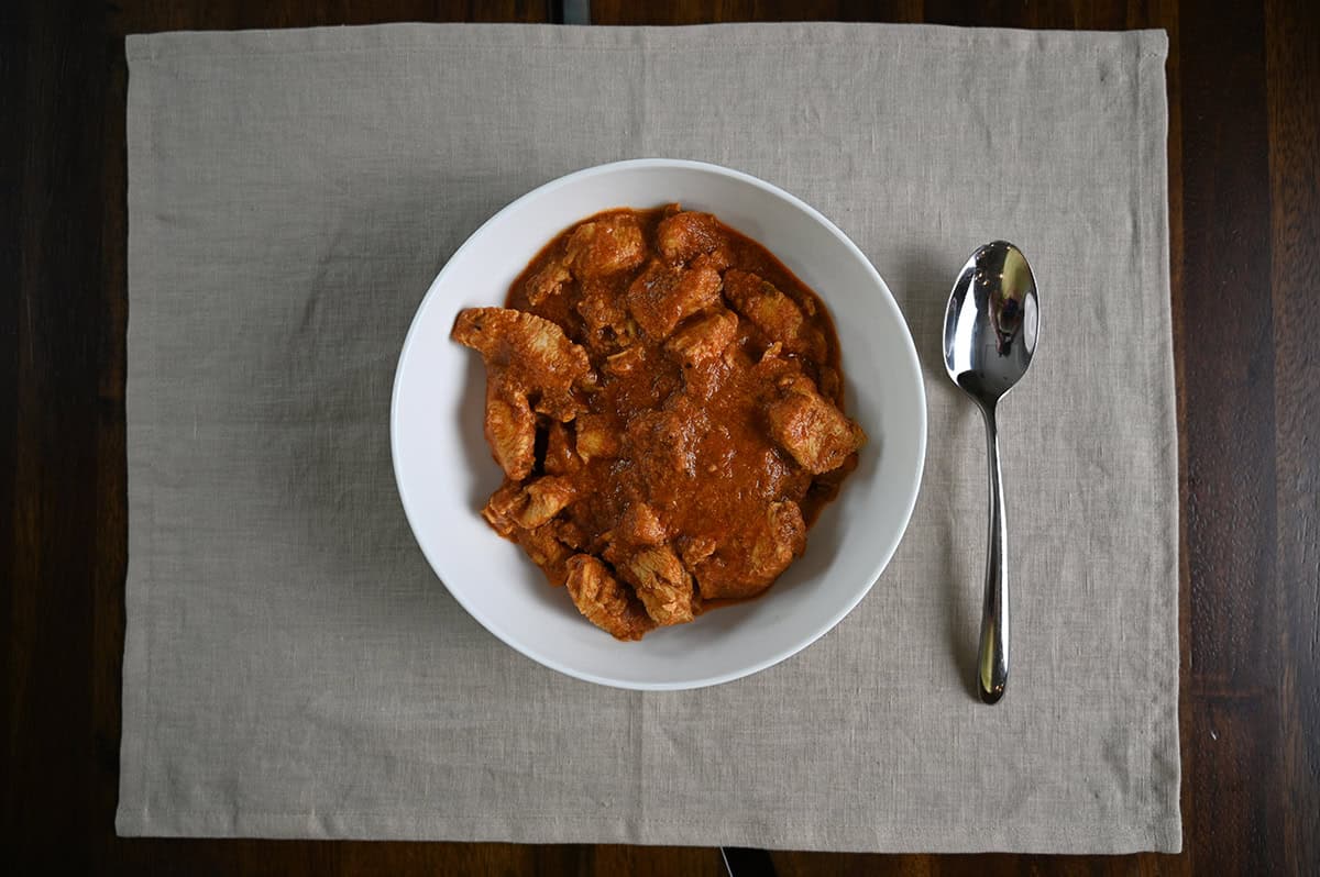 Top down image of a bowl of tikka masala with a spoon resting beside the bowl.