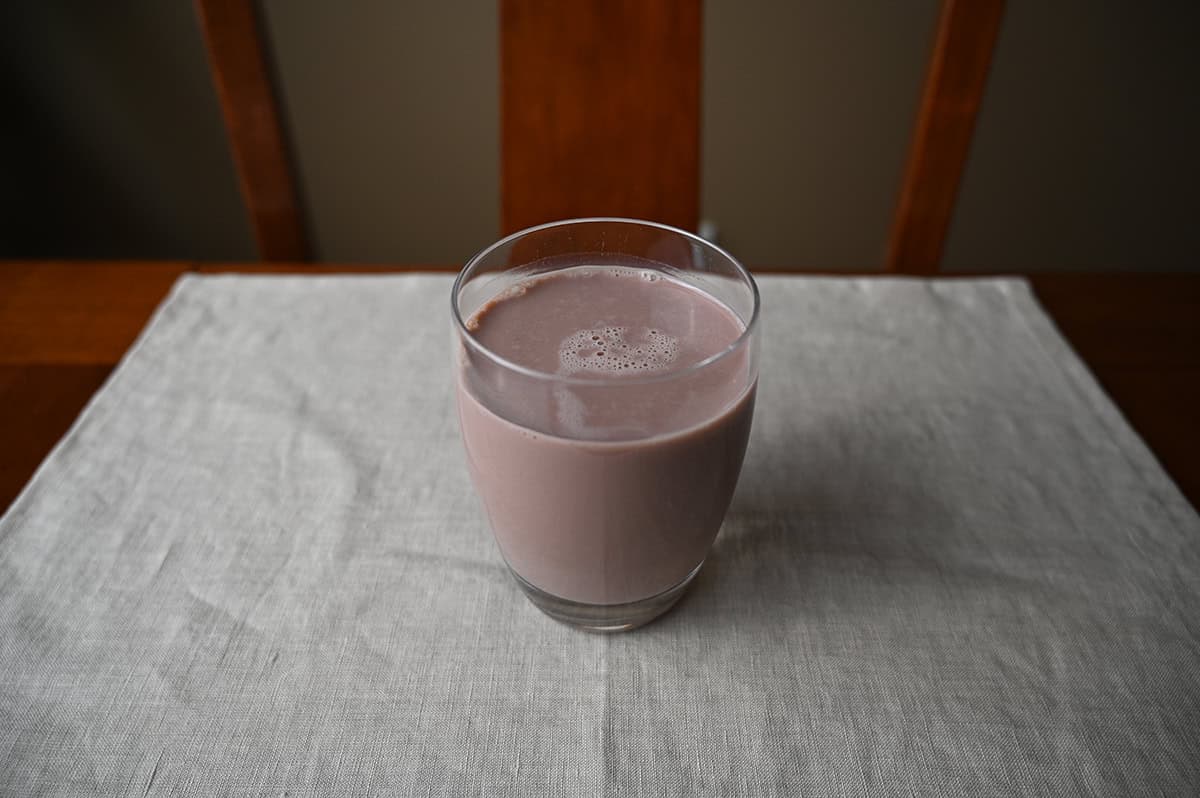 Image of a clear glass sitting on a table with chocolate protein shake poured in it.