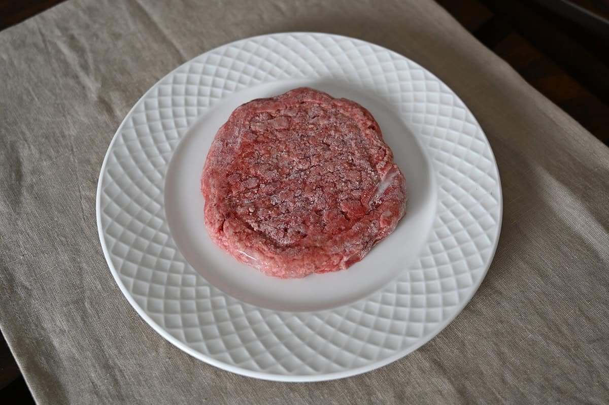 Top down image of one frozen angus ground chuck and beef patty served on a plate. 