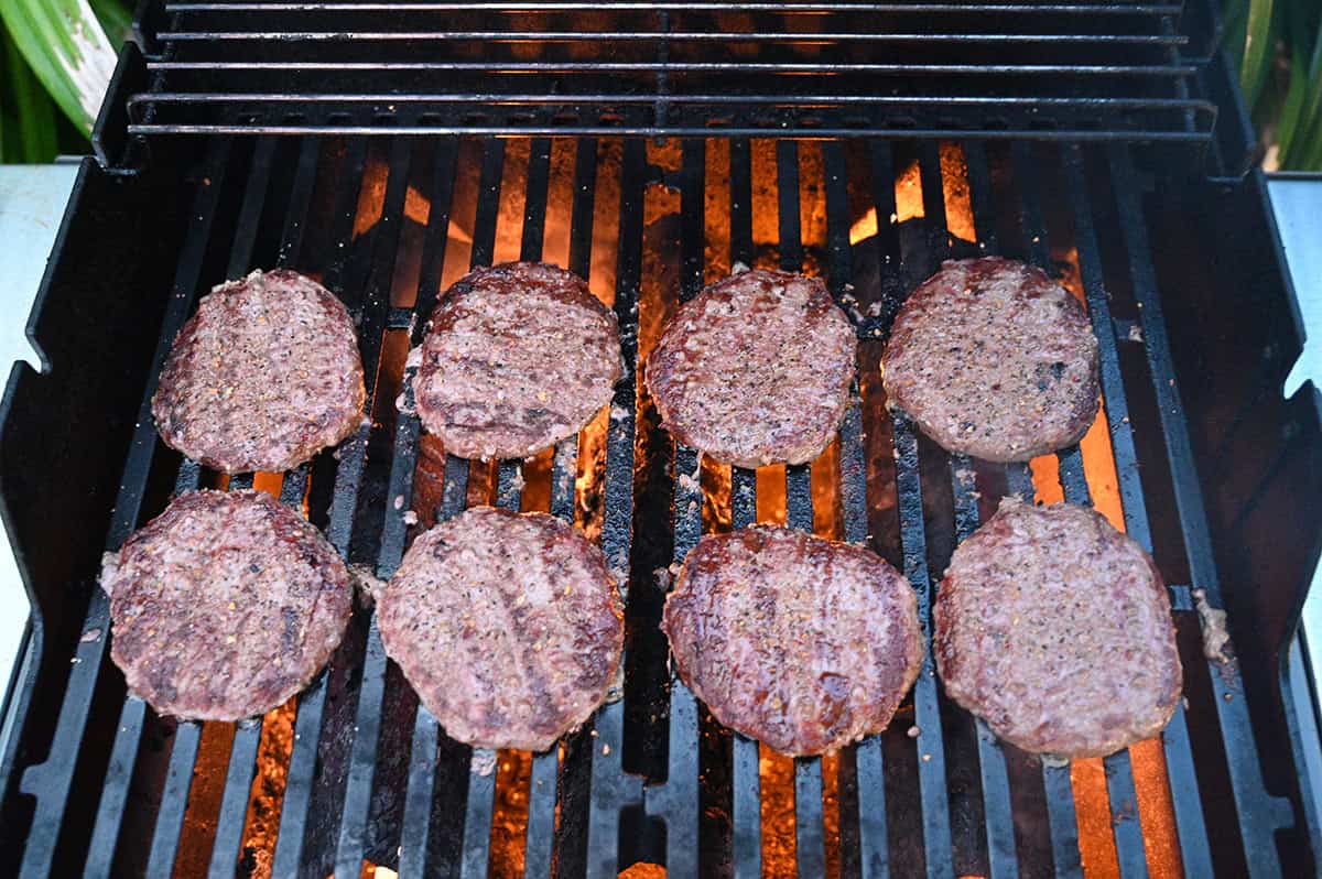 Closeup top down image of eight burger patties being barbecued. There are four grass fed on the left and four angus chuck on the right. 