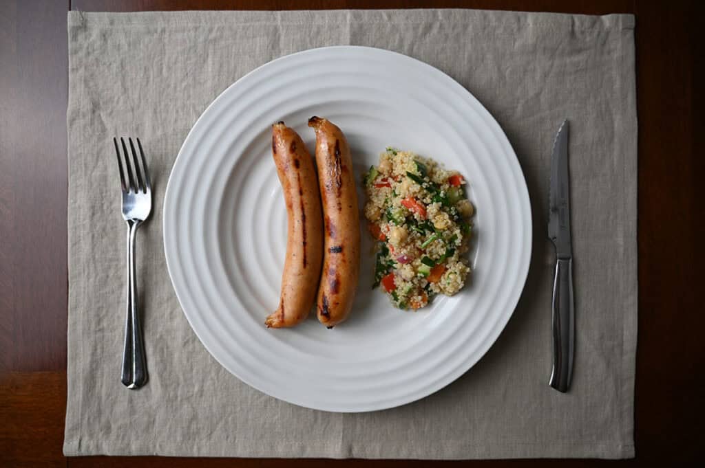 Top down image of two cooked chicken sausages beside a serving of quinoa salad.