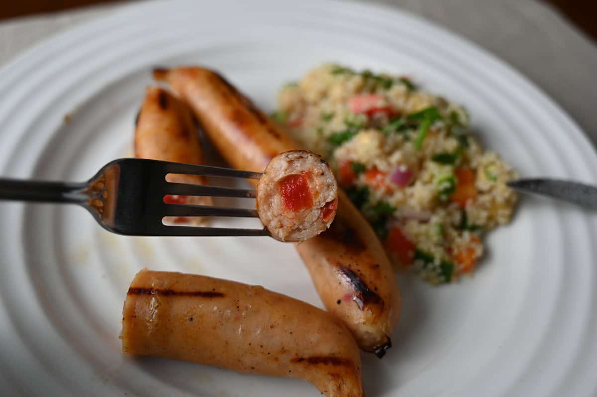 Closeup image of a fork with one slice of sausage on it so you can see the center of the sausage and a piece of red pepper in the filling. 