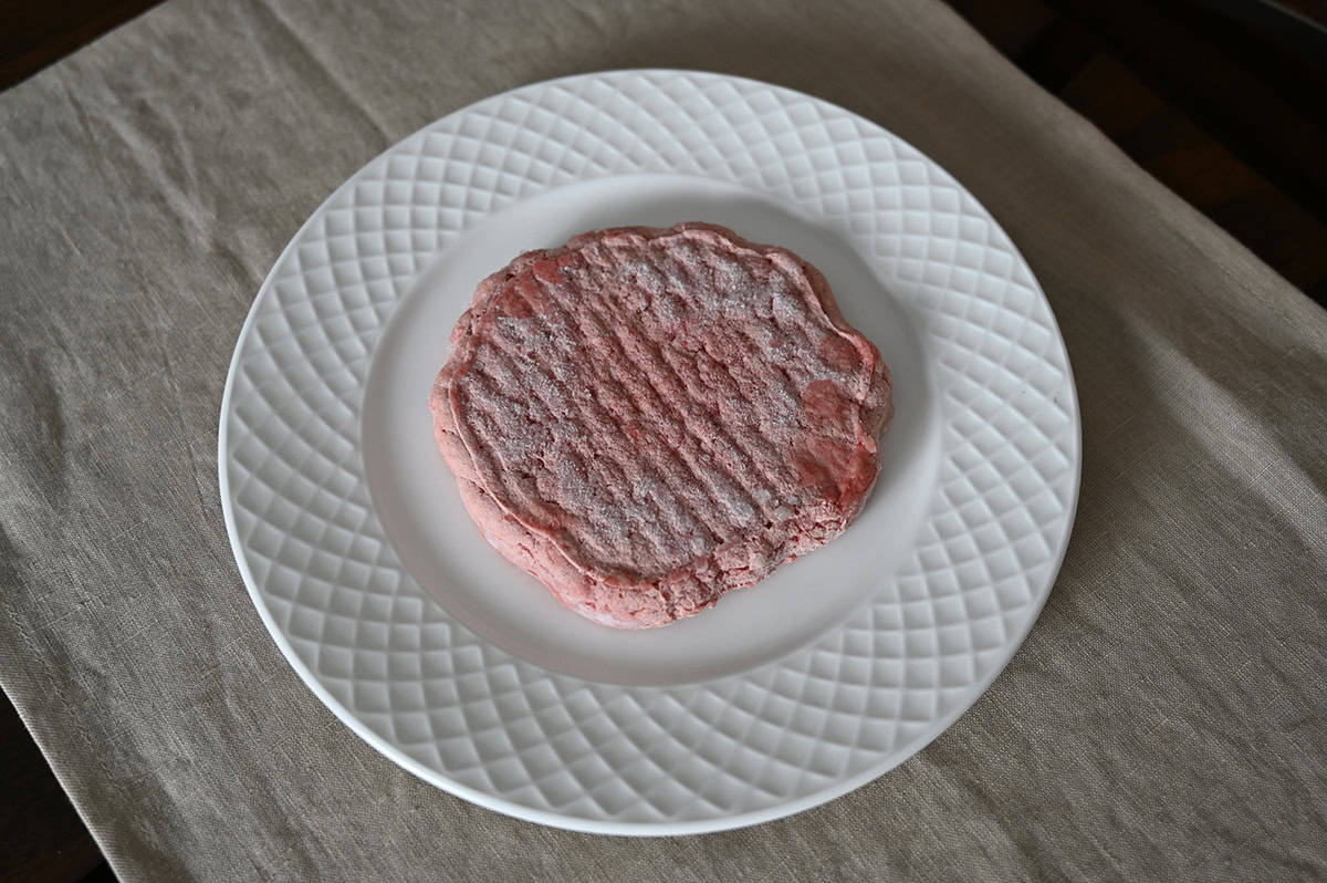 Top down image of one frozen grass-fed burger patty served on a plate. 